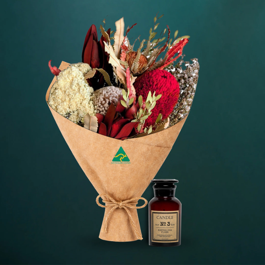Deep red dried native bouquet beside an amber glass Australian Flora soy candle, both kraft-wrapped with Australian Made stamp, on a dark teal background