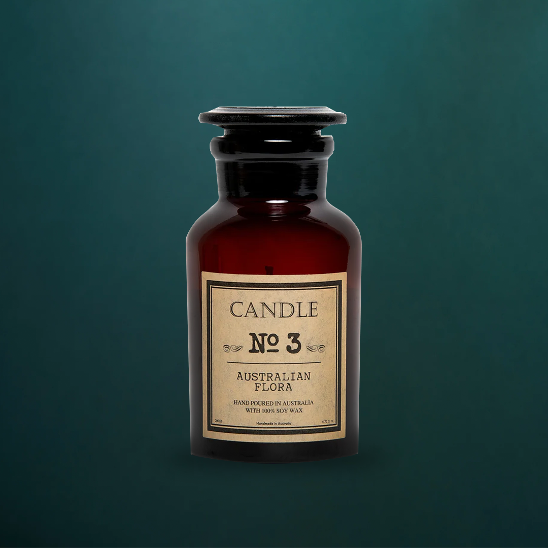 Australian Flora soy candle in an amber apothecary glass jar with a glass stopper and vintage Candle No 3 label, on a dark teal background