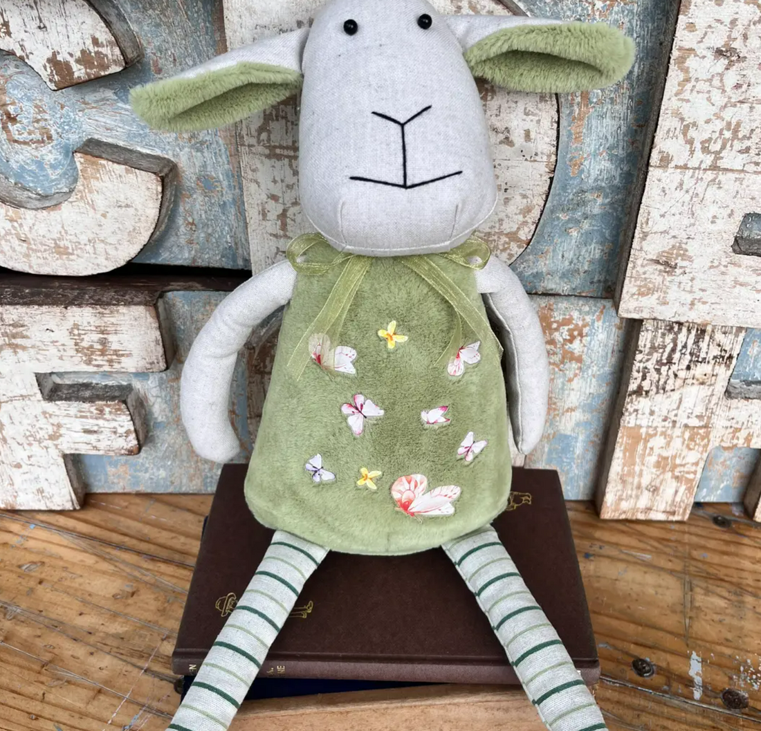 Australian-made cotton plush bunny in a sage green pinafore with appliqué butterflies and green-striped legs, sitting on a vintage book