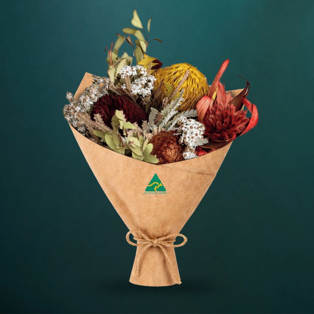 Dried Australian native bouquet in mustard tones featuring banksia formosa, deep purple banksia, tea tree foliage and white ixodia, wrapped in kraft paper