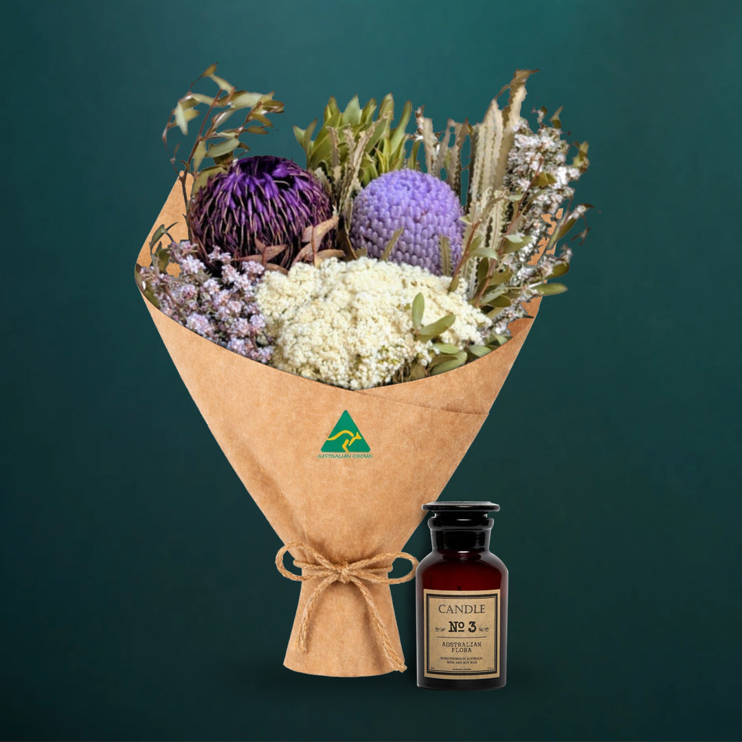 Lilac and purple dried native bouquet beside an amber glass Australian Flora soy candle, both kraft-wrapped with Australian Made stamp, on a dark teal background