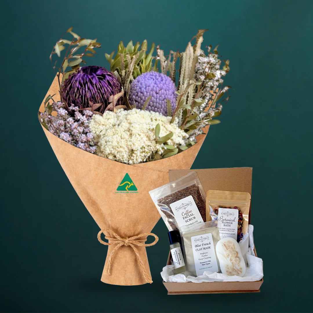 Lilac and purple dried native bouquet beside a five-piece Butler Bath pamper set in a kraft gift box with coffee scrub, clay mask, soap and flower bath, on dark teal