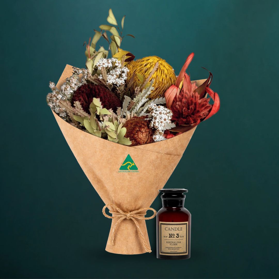 Mustard dried native bouquet beside an amber glass Australian Flora soy candle, both wrapped in kraft with Australian Made stamp, on a dark teal background