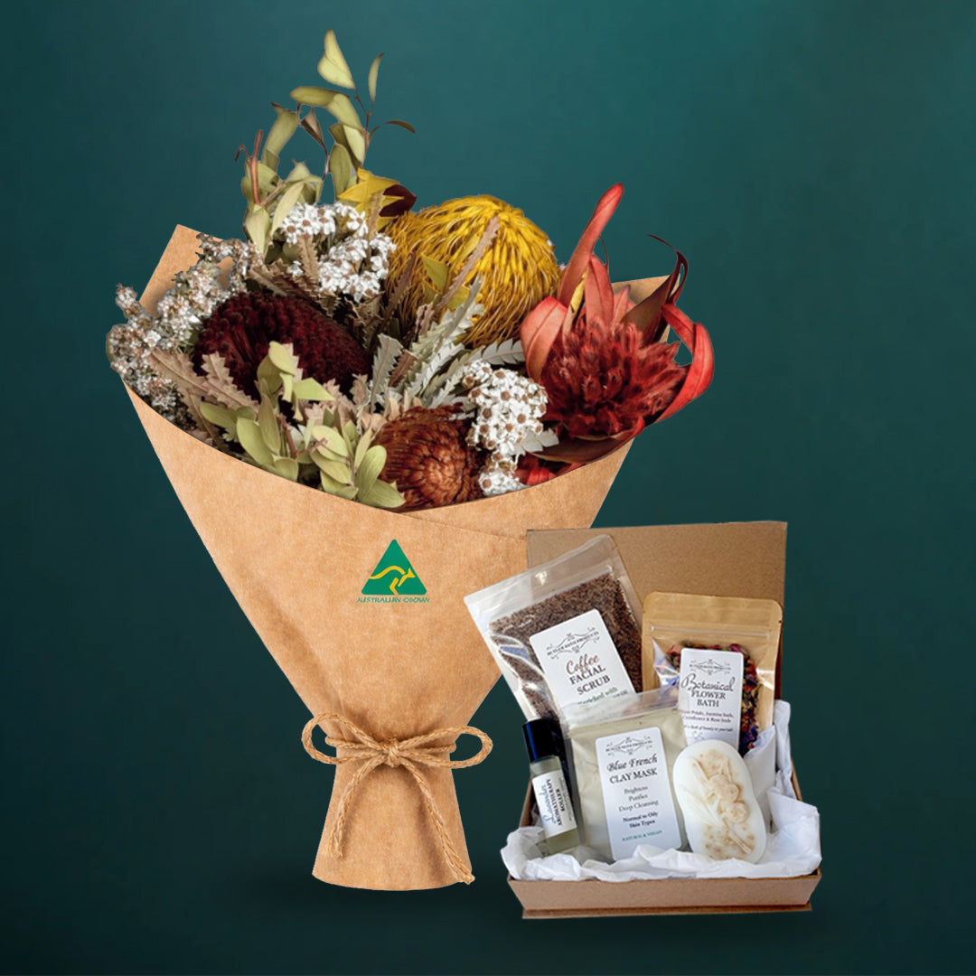 Mustard dried native bouquet beside a five-piece Butler Bath pamper set in a kraft gift box with coffee scrub, clay mask, soap and flower bath, on dark teal