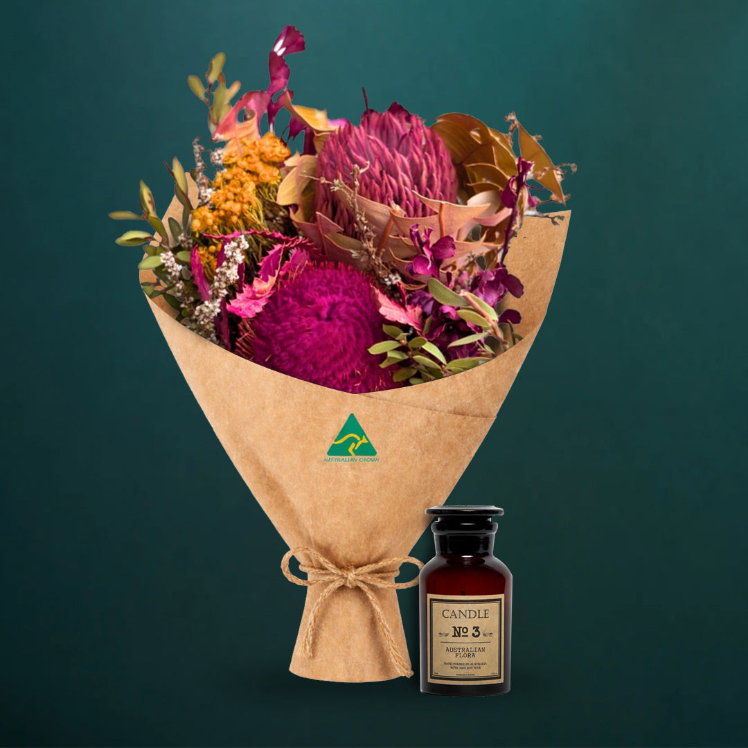 Hot pink dried native bouquet beside an amber glass Australian Flora soy candle, both kraft-wrapped with Australian Made stamp, on a dark teal background