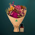 Hot pink dried native bouquet beside an amber glass Australian Flora soy candle, both kraft-wrapped with Australian Made stamp, on a dark teal background
