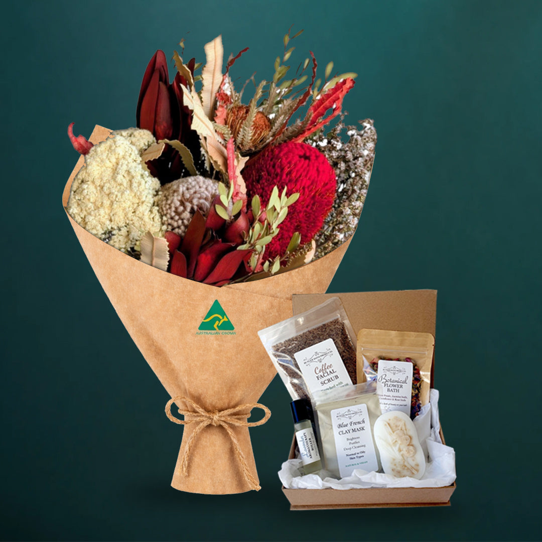 Deep red dried native bouquet beside a five-piece Butler Bath pamper set in a kraft gift box with coffee scrub, clay mask, soap and flower bath, on dark teal